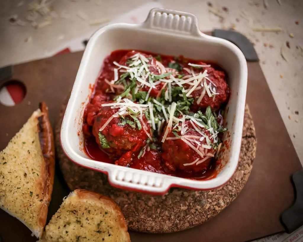 Meatballs in red sauce, topped with cheese and herbs, with garlic bread.