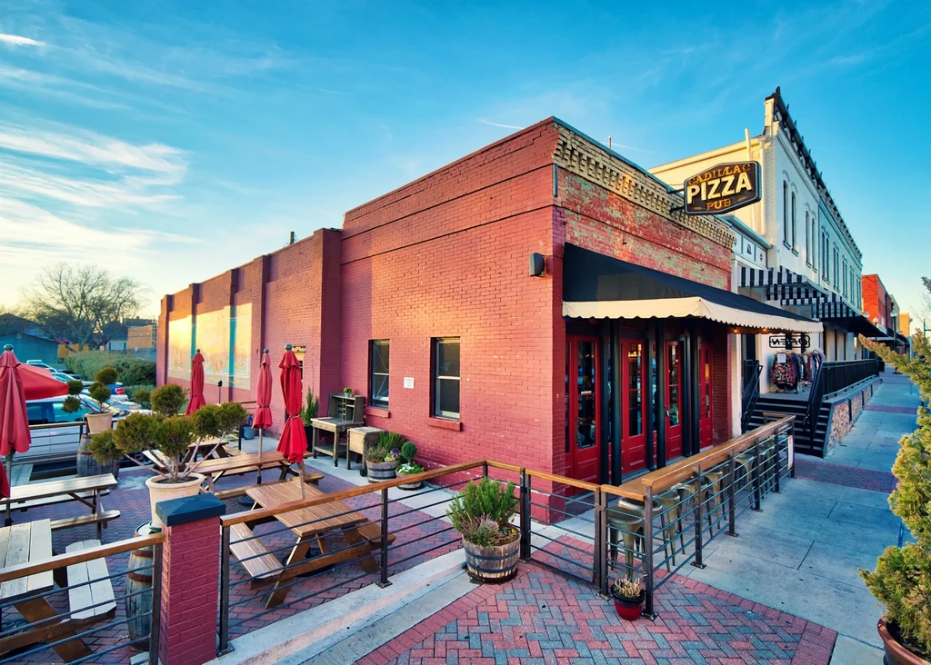 Brick Cadillac Pizza Pub building with outdoor patio and red umbrellas.