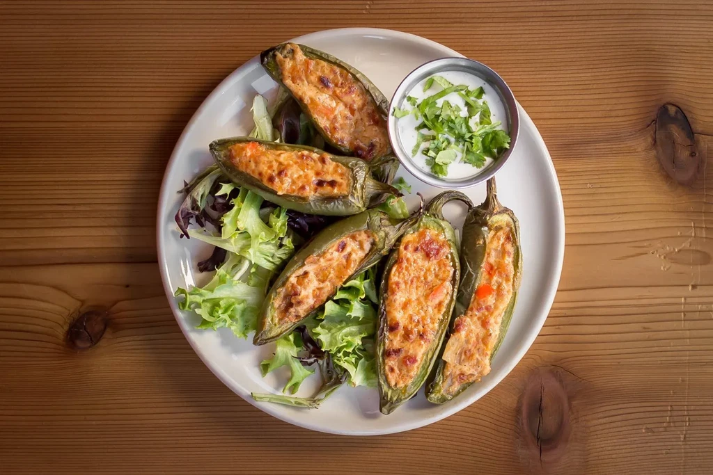 Baked stuffed jalapeño peppers on greens, with herb-garnished dipping sauce.