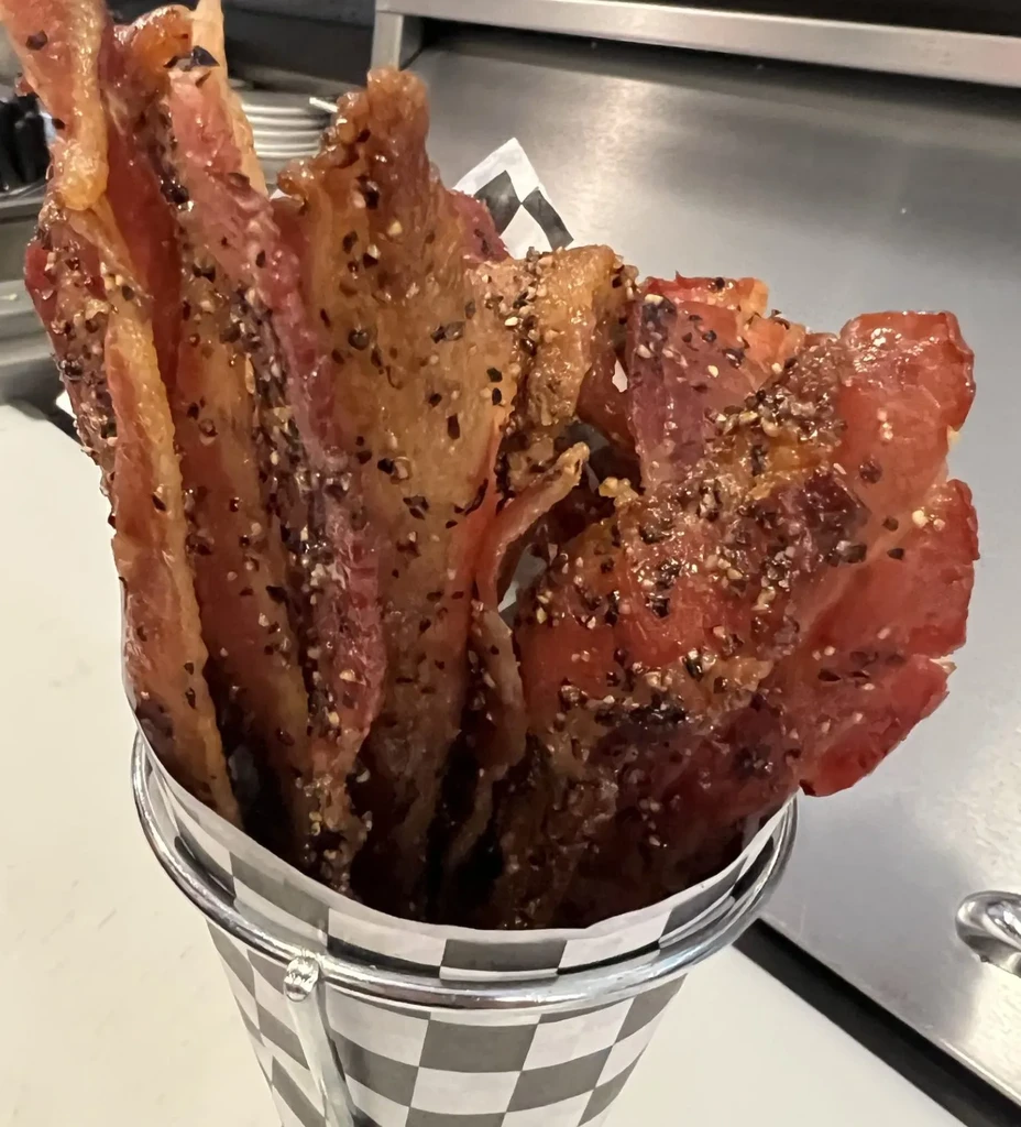 Upright strips of glossy, peppered bacon in a checkered metal bucket.