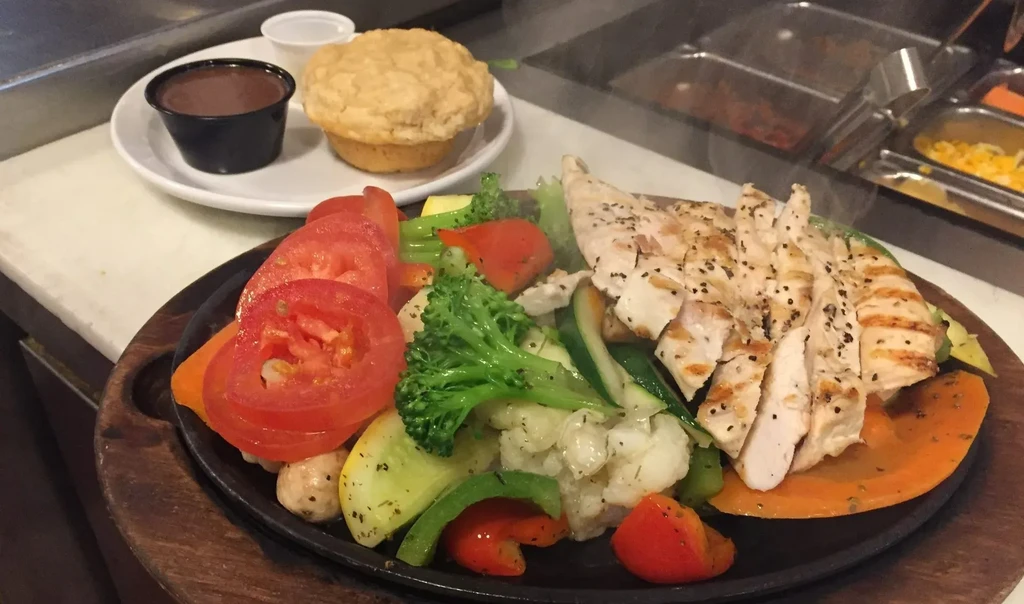 Close-up of grilled chicken and mixed vegetables steaming on a hot plate.