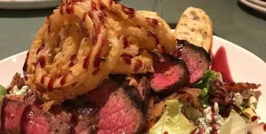 Sliced medium-rare steak salad topped with a large onion ring.