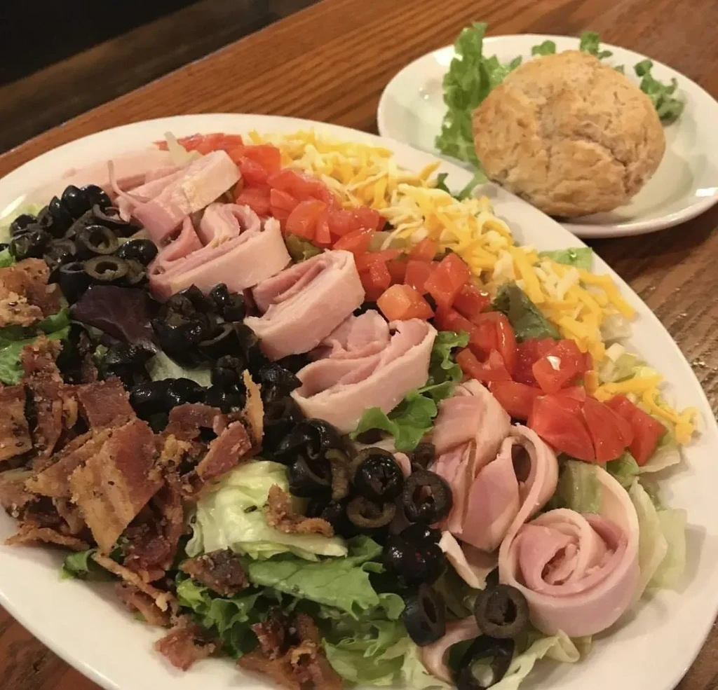 Colorful salad with ham rosettes, bacon, olives, cheese, and tomatoes.