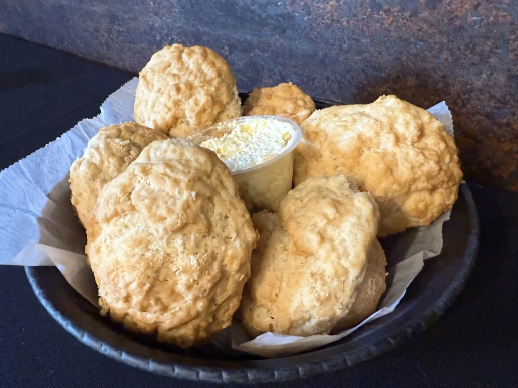 Rustic golden biscuits in dark basket with butter and cheese topping.