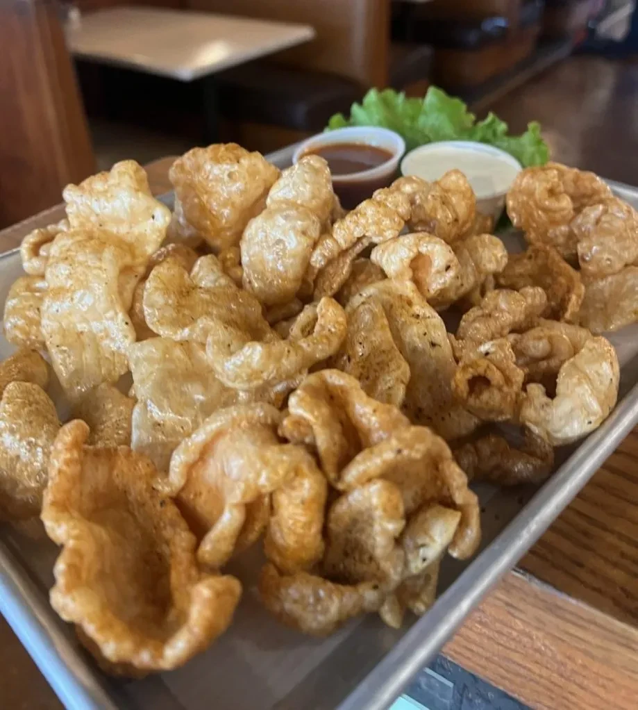 Crispy chicharrónes piled on a tray with two sauces and garnish.