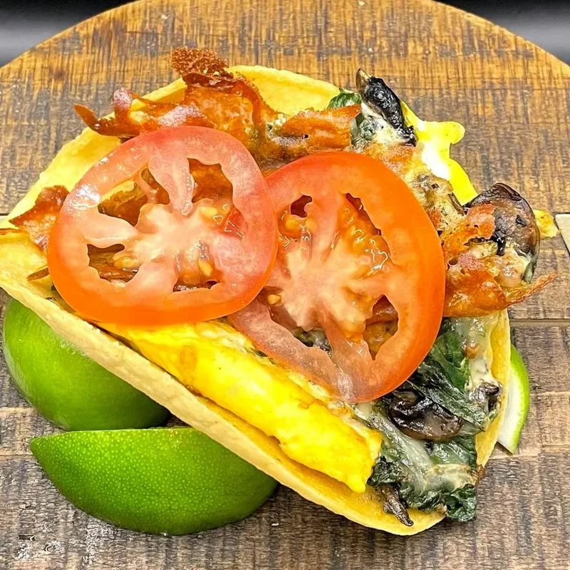 Breakfast taco with egg, spinach, mushrooms, bacon, tomato, and lime.