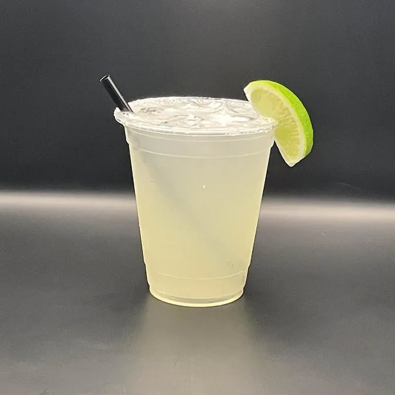 Plastic cup with iced lime drink, black straw, and lime wedge.