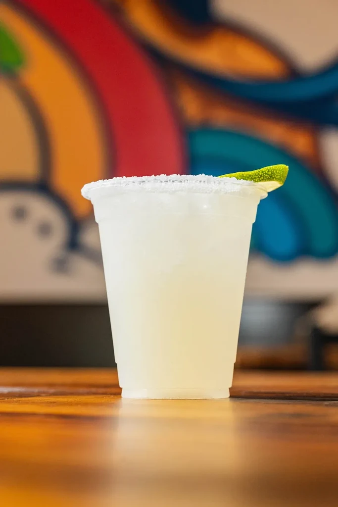 Close-up of a salt-rimmed frozen margarita with lime on wood.