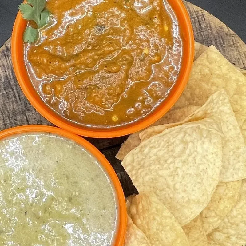 Top-down: two bowls of dip and tortilla chips on wood.