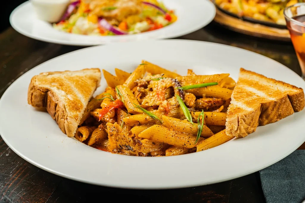 Penne pasta in reddish sauce, topped with green onions and toast.