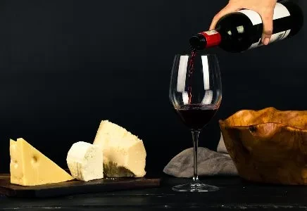 Still life: red wine pours into glass with assorted cheeses.