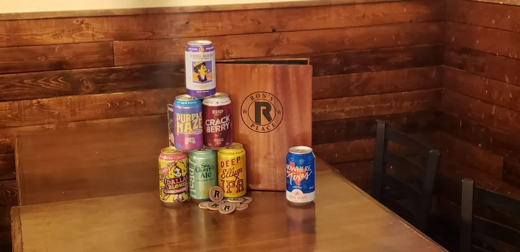Eight stacked beer cans, a 'RON'S PLACE' sign, and 'R' tokens.
