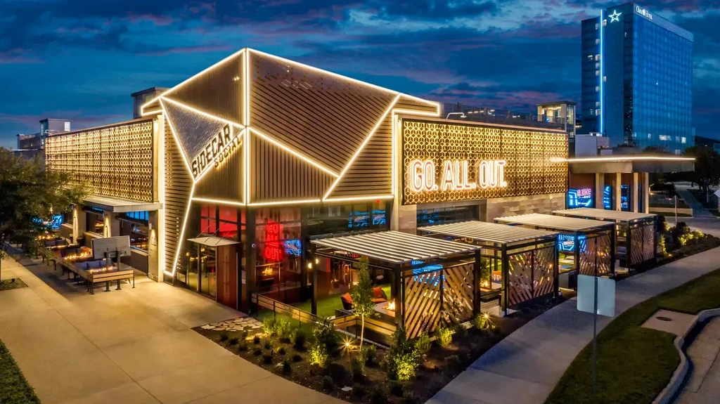 SIDECAR SOCIAL: an angular, brightly lit building with outdoor seating at dusk.