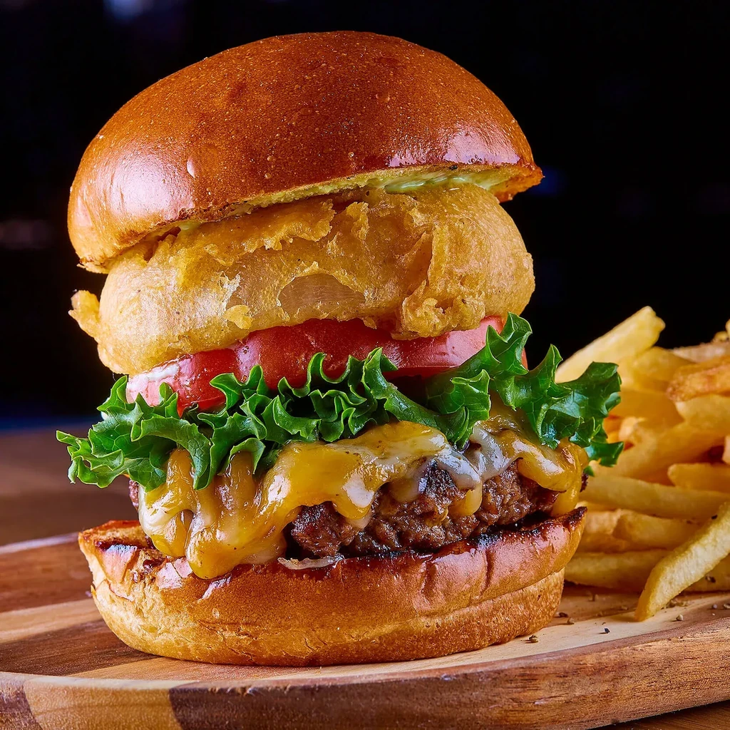 A beef burger with melted cheese, a large onion ring, and fries.