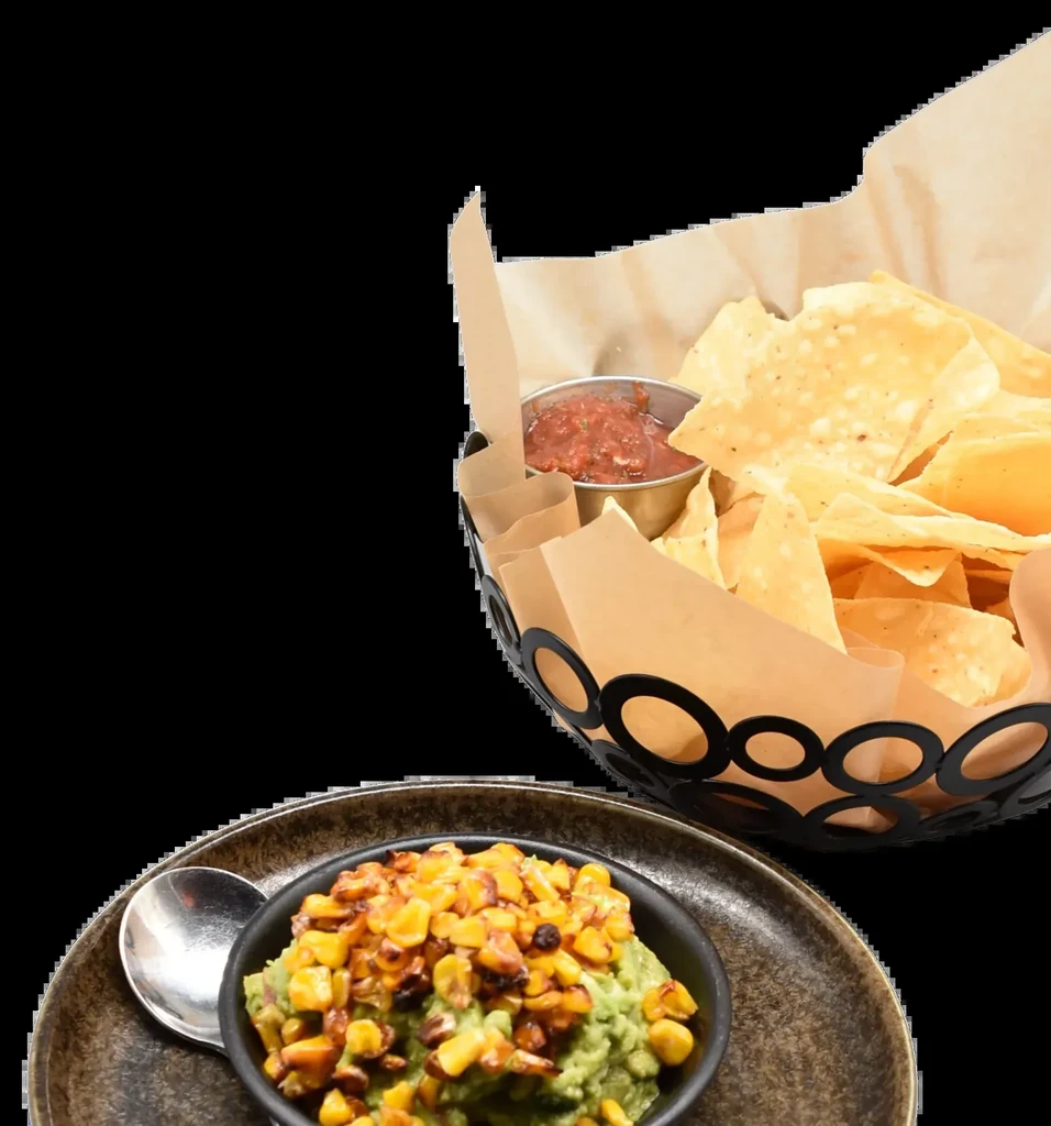 Guacamole with corn in bowl, chips and salsa against black.