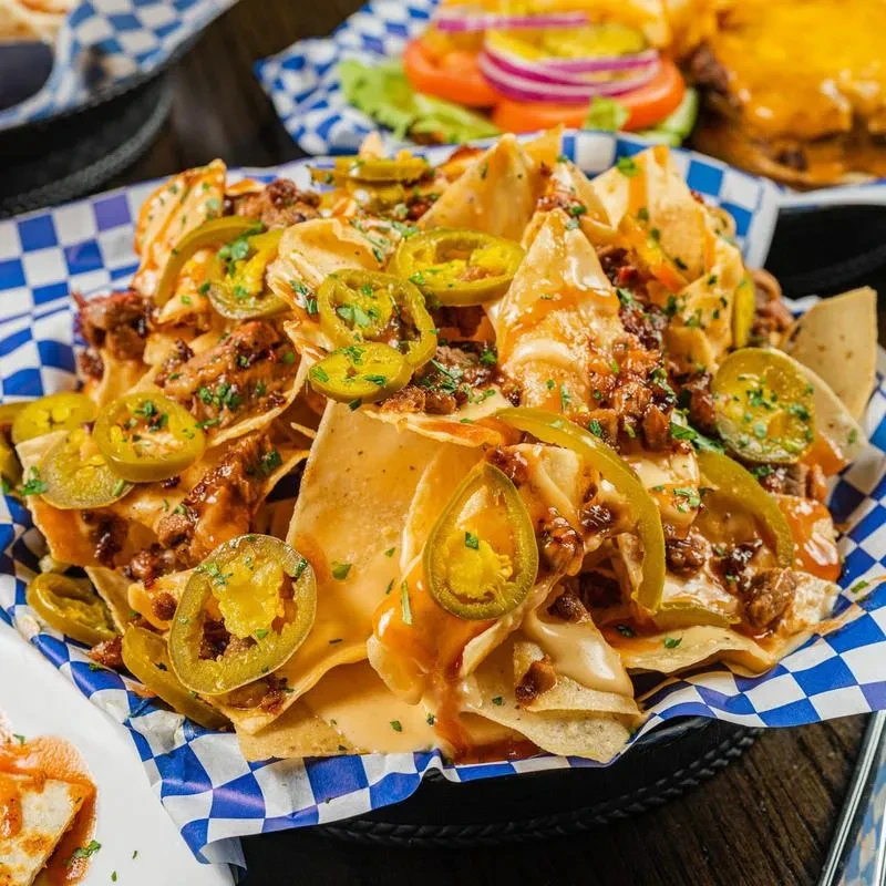 Close-up of crispy nachos with cheese, seasoned meat, jalapeños, and herbs.
