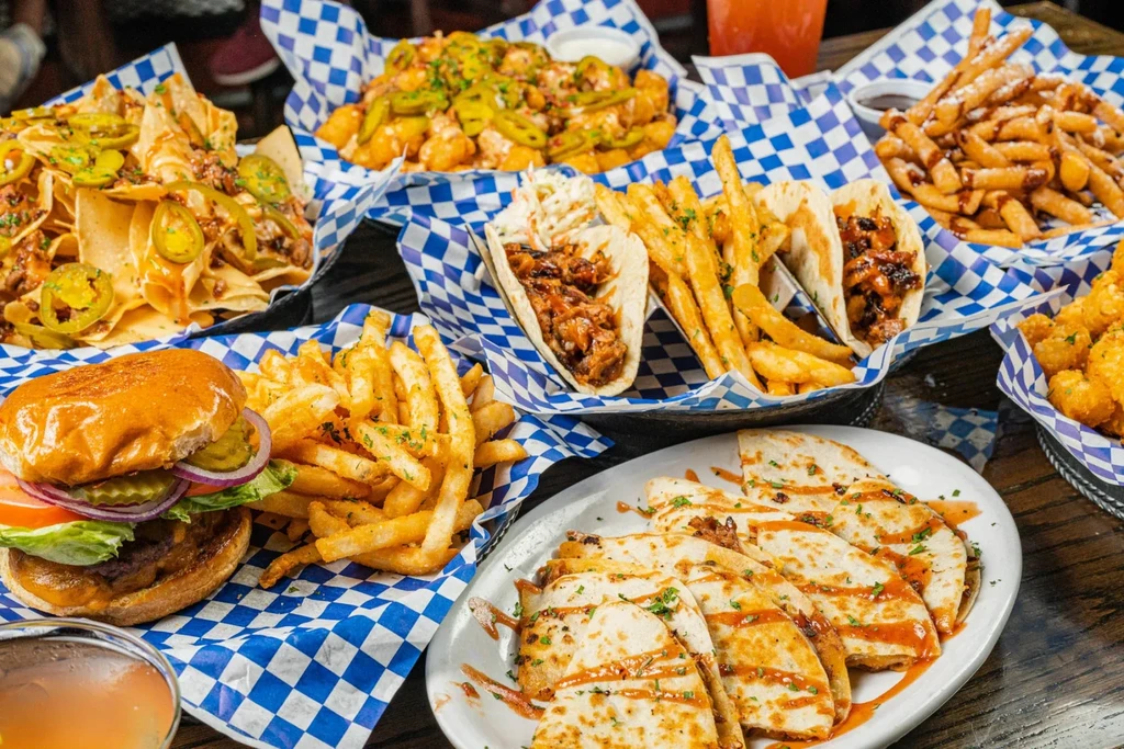 Rustic table laden with burgers, tacos, nachos, and fries.