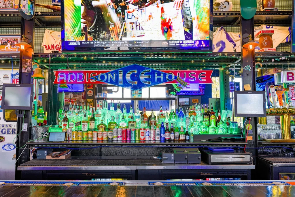 Vibrant sports bar with 'ADDISON ICE HOUSE' neon sign and sports on TV.