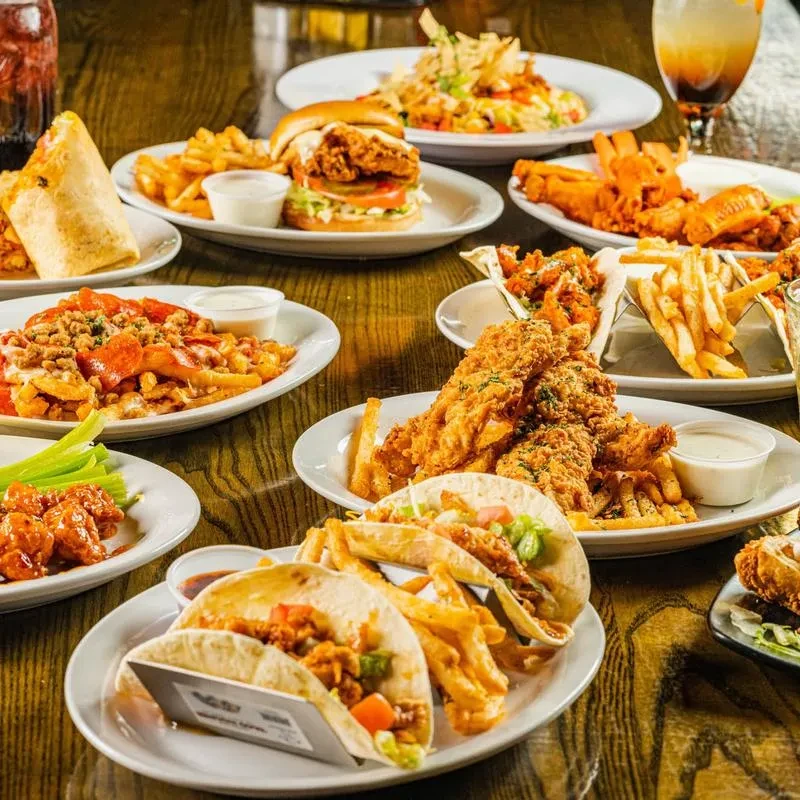 Many plates of fried chicken, tacos, fries, wings, and a burrito.