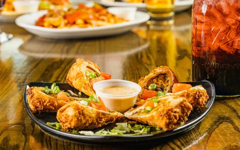 Crispy golden-brown fried rolls, cut in half, with dipping sauce and garnishes.