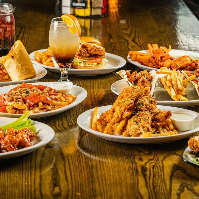 Multiple plates of casual food including fried items, a burger, and drinks.
