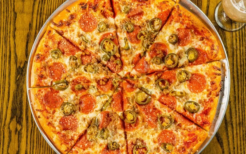 Freshly baked, pre-sliced pizza with pepperoni, sausage, jalapeños, and white cheese.