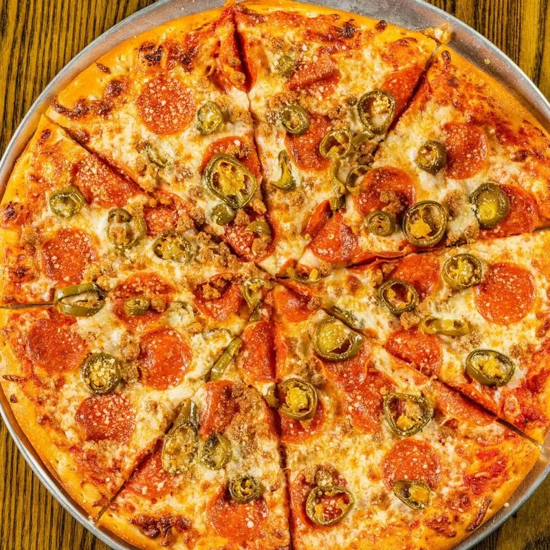 Baked pizza with melted cheese, pepperoni, sausage, jalapeños on a pan.