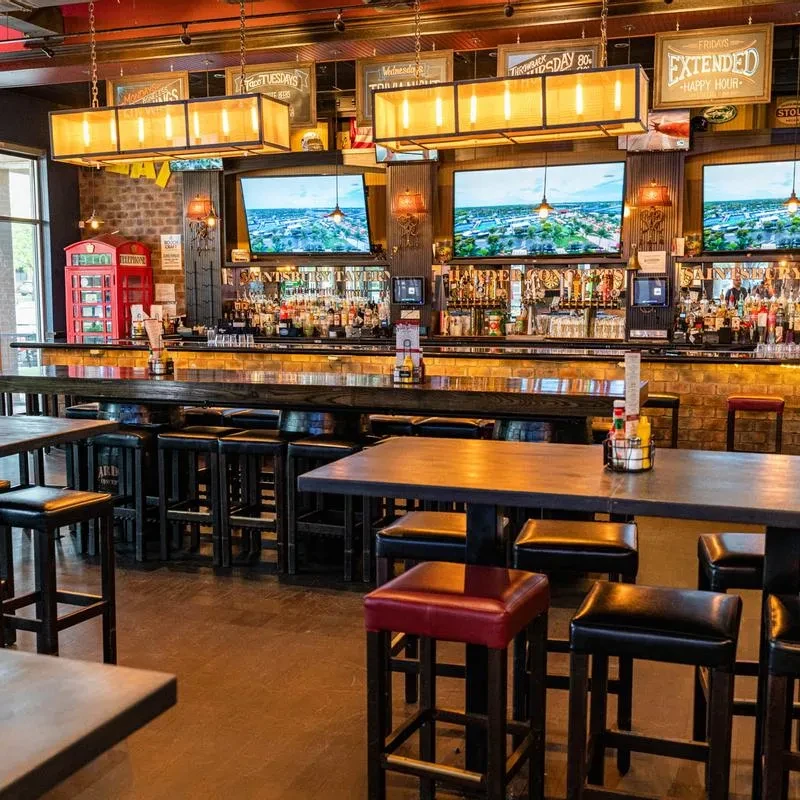 Contemporary bar with long counter, illuminated bottles, TVs, and decor.