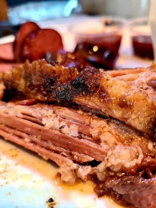 Close-up: Juicy barbecued meat with char marks, smoked sausage, and sauces.