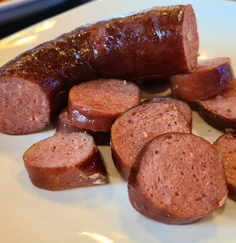 Dark reddish-brown sausage, whole and sliced, on a white plate.