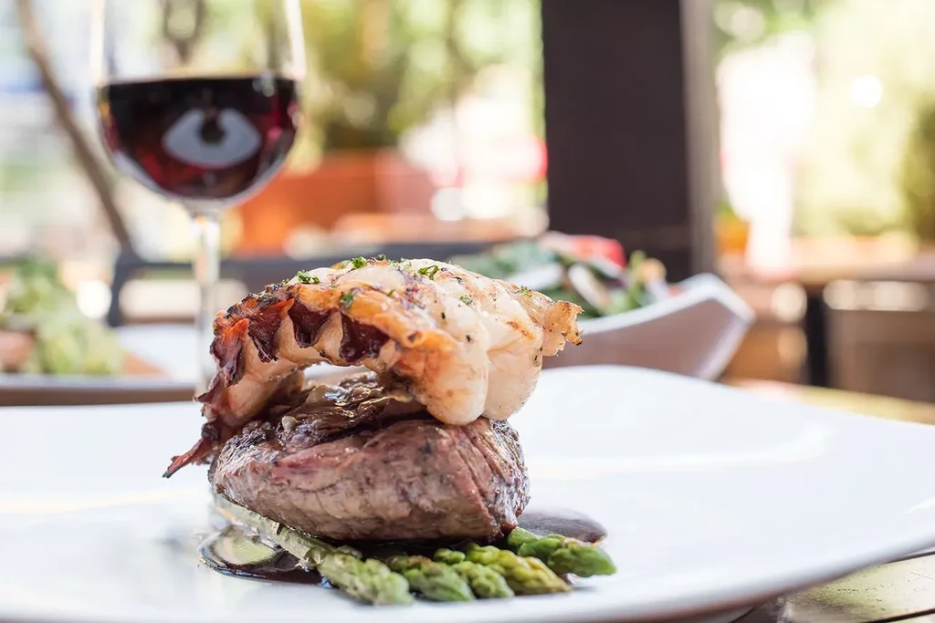 A plate of steak, grilled seafood, asparagus, herbs, and dark sauce.