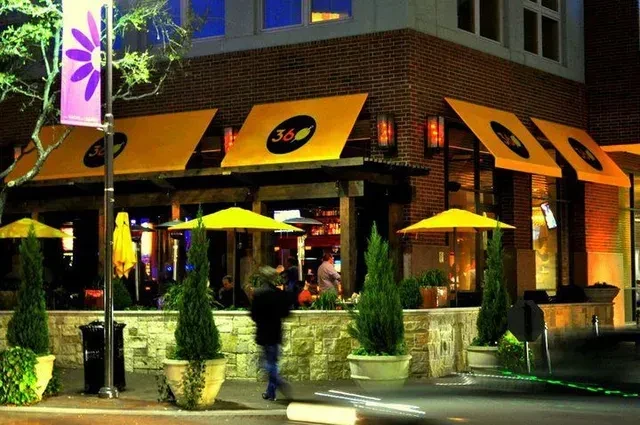 Nighttime brick restaurant with yellow awnings, outdoor patio, and blurred people.