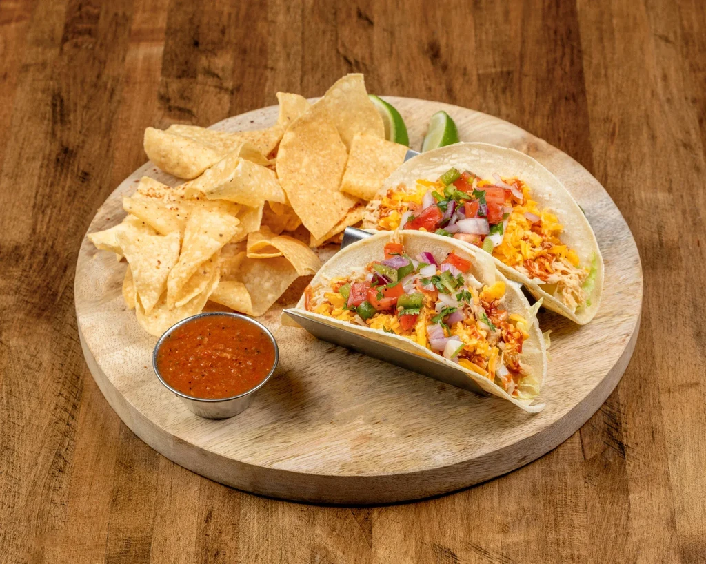 Two soft-shell tacos, chips, salsa, and lime on a rustic board.