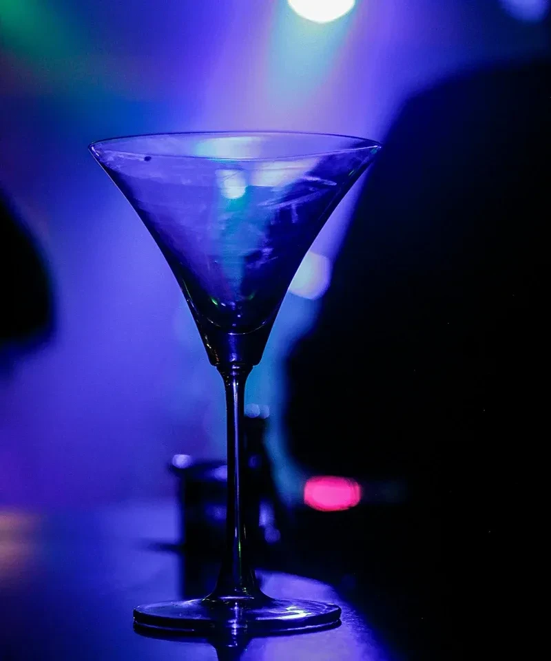 Martini glass with blue-teal drink, dark background, colorful bokeh lights.