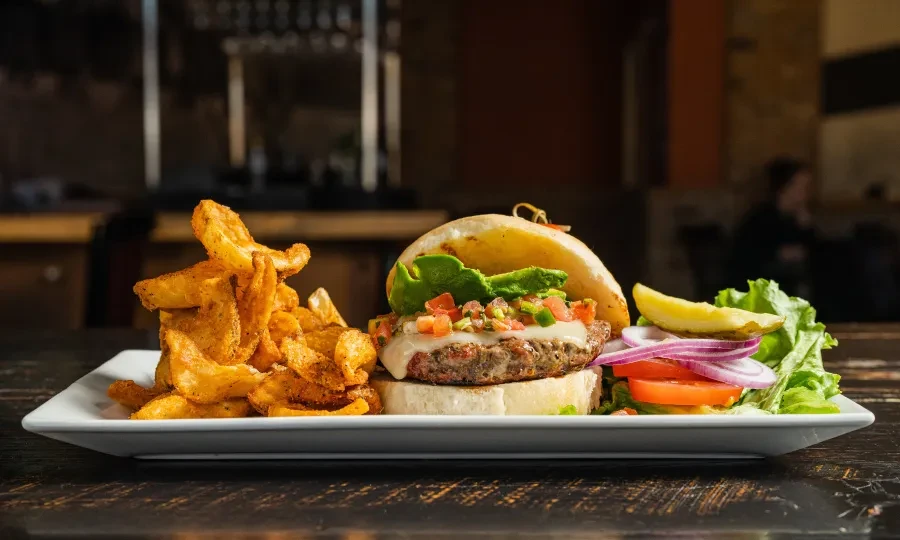 Gourmet burger with salsa, avocado, and seasoned wedges on a plate.