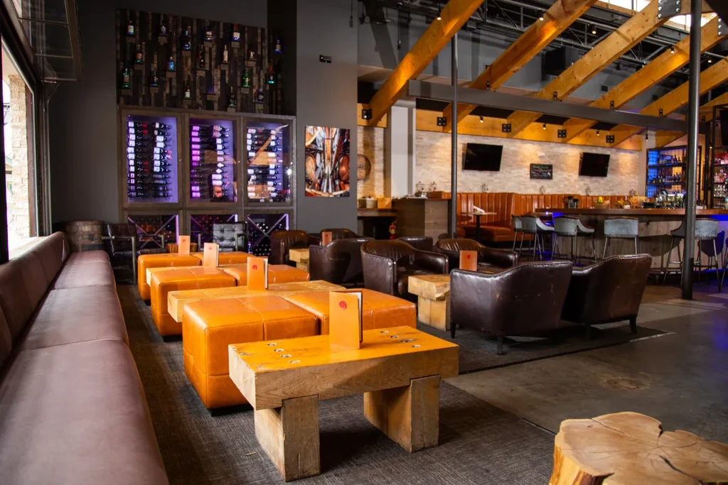 Modern restaurant interior with diverse seating, illuminated bar, and wine display.