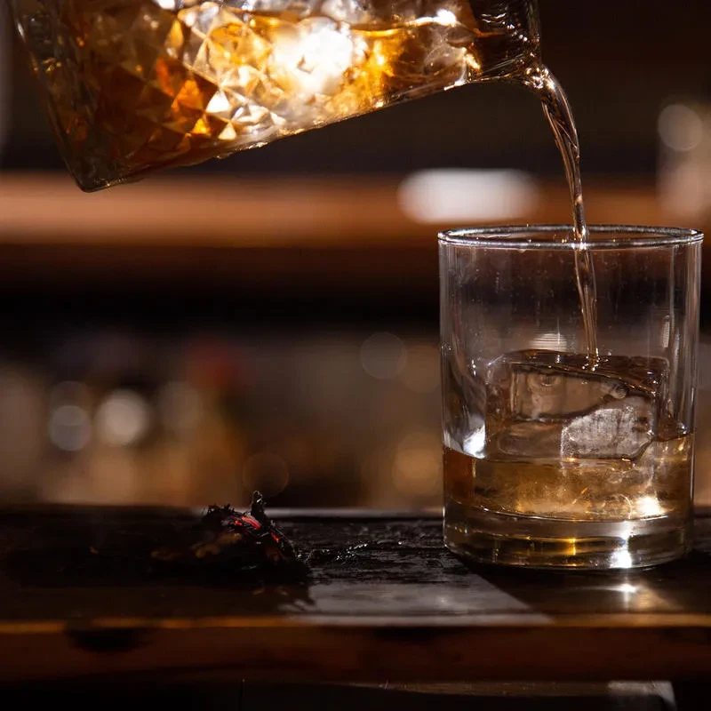 Whiskey pours into a rocks glass with a large square ice cube.