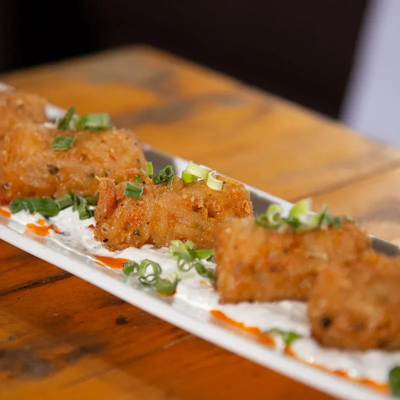 Crispy fried food with green onions and two sauces on a white plate.