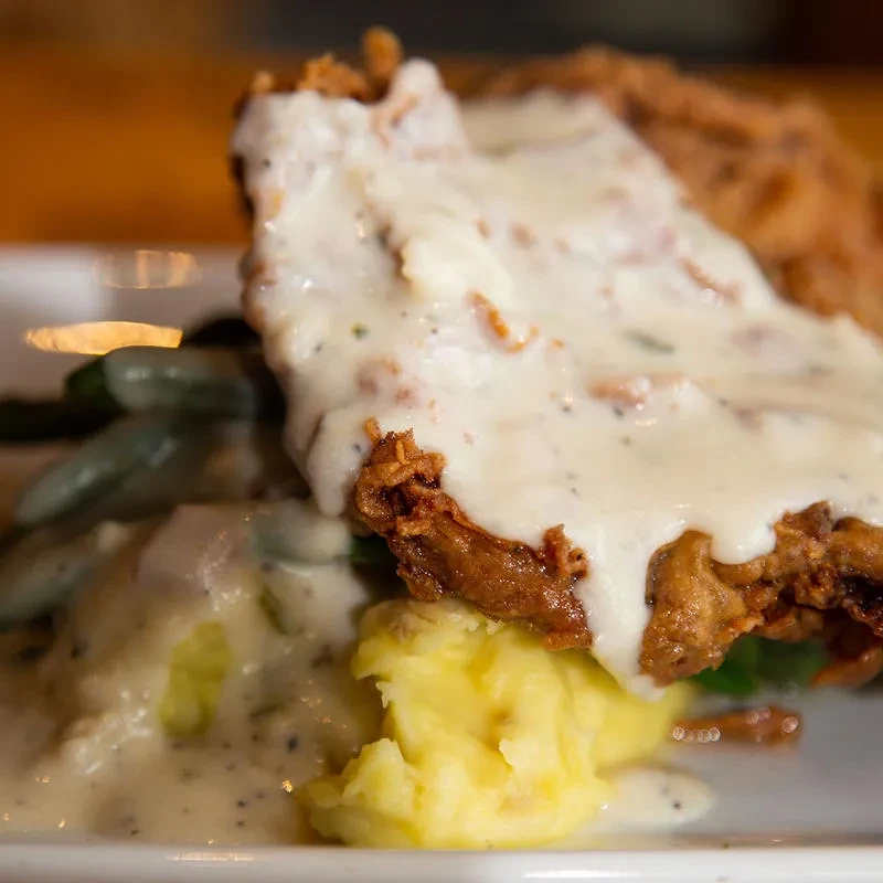 Fried breaded meat, mashed potatoes, and green beans covered in white gravy.