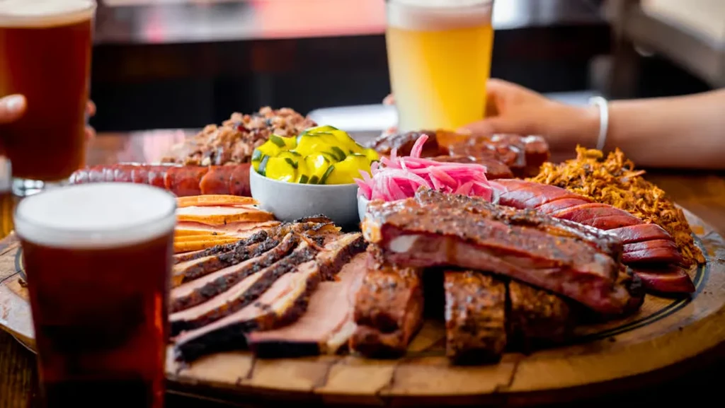 Platter of assorted BBQ meats, beans, pickles, and two beers.