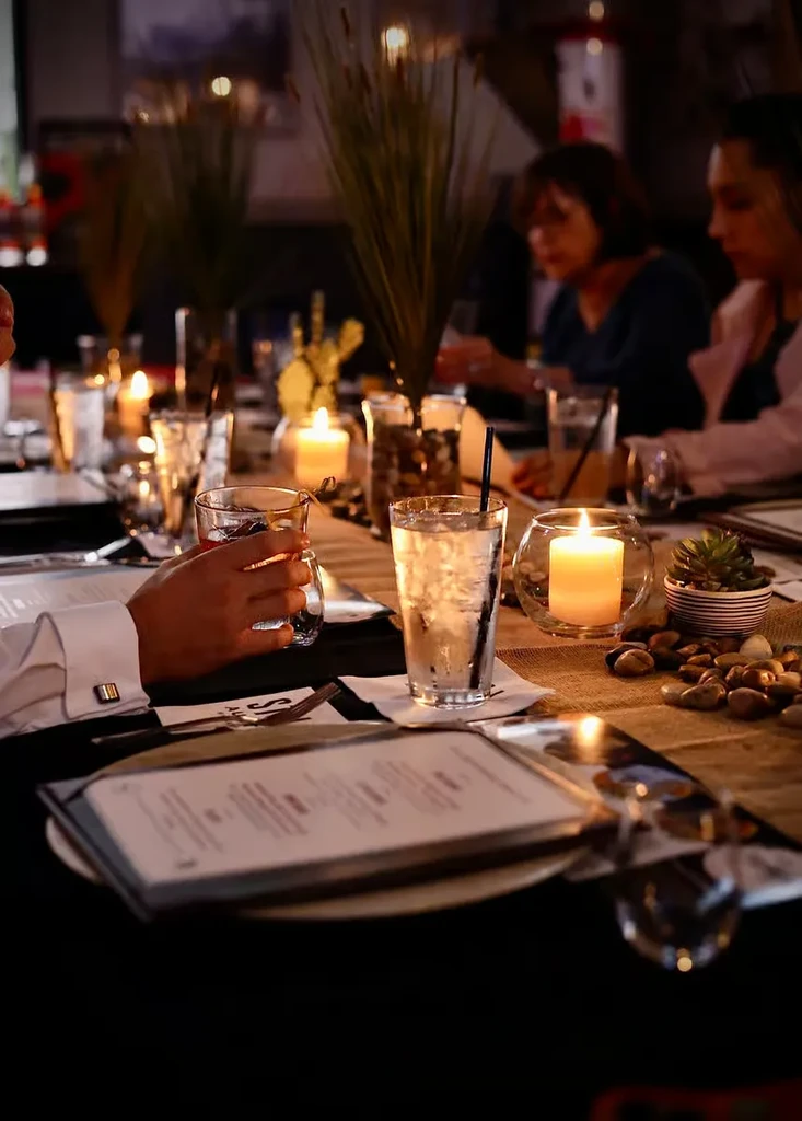 Hands holding a drink at a warm, elegant candlelit table.