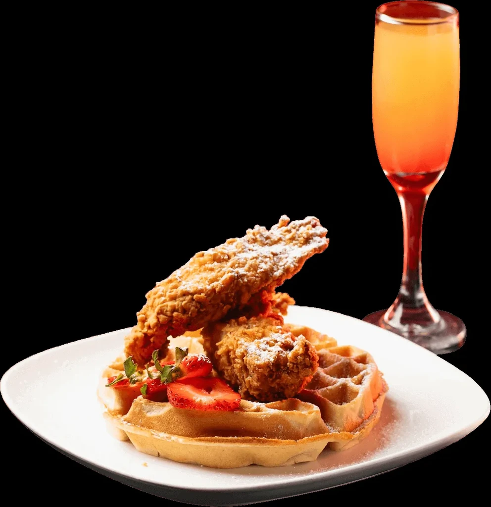Chicken and waffles with strawberries, greens, and a mimosa on black background.