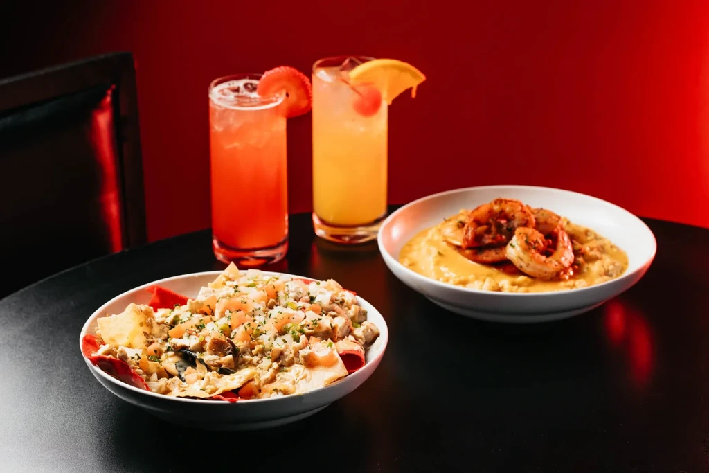Nachos, shrimp and grits, two cocktails, dark table, red background.