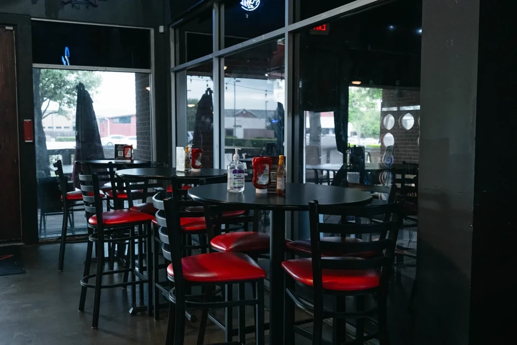 Empty restaurant with dark high-top tables, red stools, and condiments.