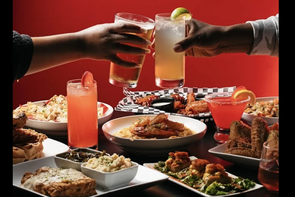 Hands toasting drinks over a vibrant table with fried Southern dishes.