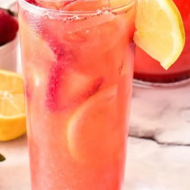Glass of cold pink lemonade with lemon, fruit, and condensation.