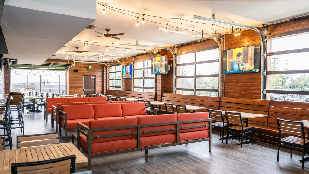 Empty rustic-industrial restaurant interior with wooden walls and reddish-orange sofas.