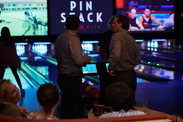 Lively "PIN STACK" bowling alley with people socializing under neon lights.