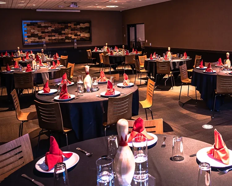 Dimly lit event space, round tables, white bowling pin centerpieces.
