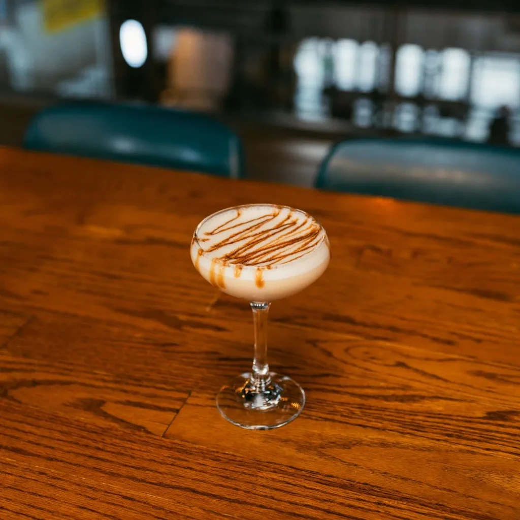 Creamy frothy cocktail in a coupe glass with striped caramel drizzle.